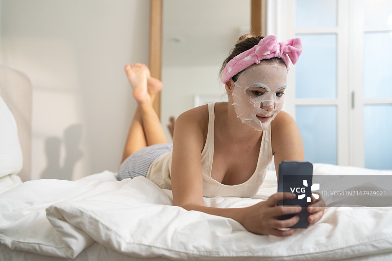 女子在家中客厅敷面膜，使用智能手机图片素材
