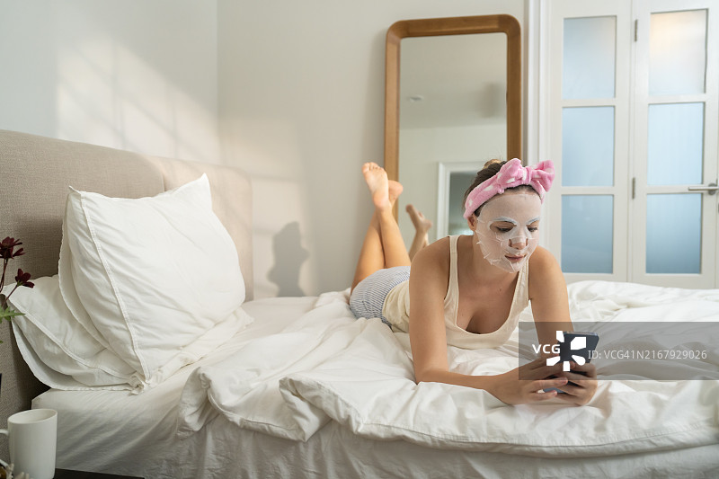 女子在家中客厅敷面膜，使用智能手机图片素材
