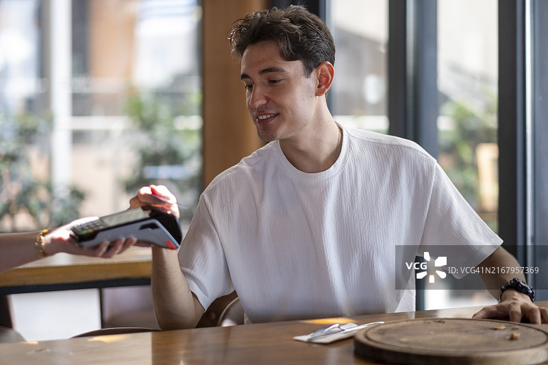 年轻男人在餐厅用信用卡进行非接触式支付图片素材