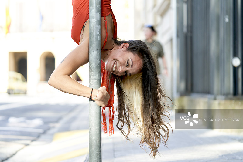 一位漂亮的女人在街头钢管上跳钢管舞，面带微笑，穿着圣费尔明服装，侧面图片素材