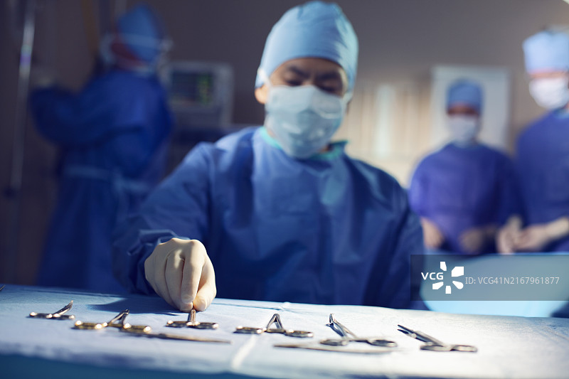 护士整理手术医疗器械工具的手，戴着手套准备在医院手术室进行手术，与同事团队合作图片素材