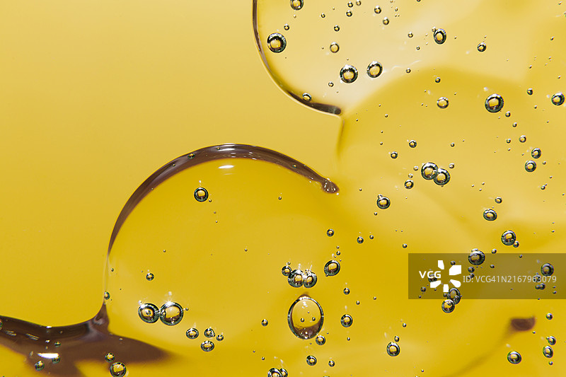 黄色背景上带有气泡的透明凝胶或精华液化妆品纹理，透明质酸液体凝胶图片素材