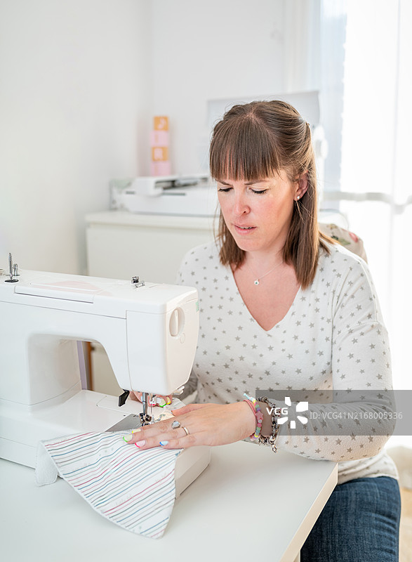 在明亮的家庭工作室里专注缝纫的女人图片素材