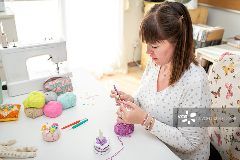 女人在明亮的工作区，用紫色纱线在桌子上钩针编织图片素材