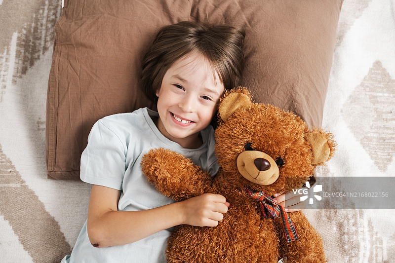 白人男孩躺在床上抱泰迪熊微笑图片素材