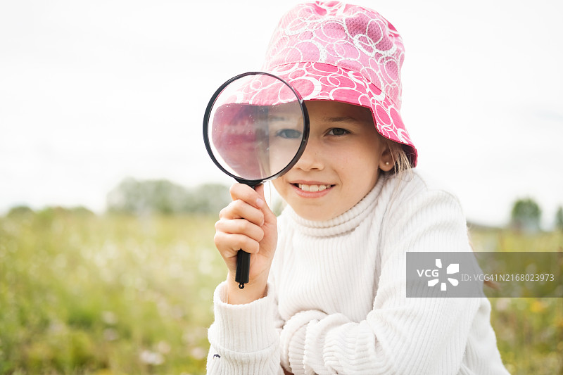 夏天，在田野里，小女孩透过放大镜看着镜头，微笑着图片素材