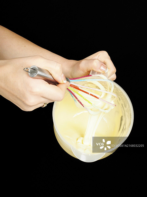 女人用手动打蛋器在塑料碗里做格戈尔-莫格尔，黑色背景图片素材