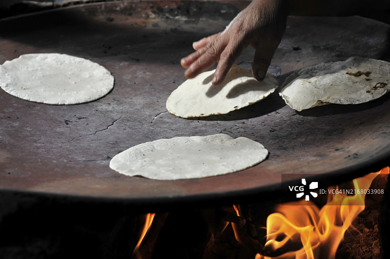 墨西哥瓦哈卡州米特拉，中美洲，在明火上烤玉米饼，一只手翻动玉米饼图片素材