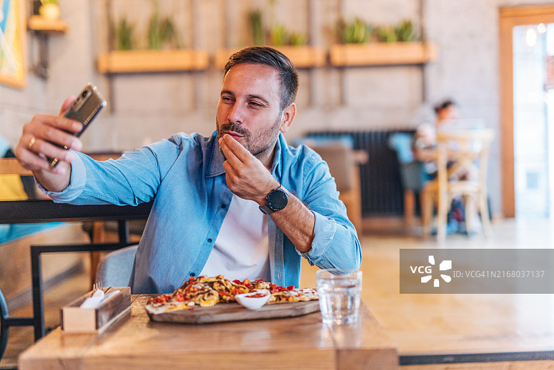 餐厅里快乐的英俊中年男人正在拍摄他的披萨图片素材