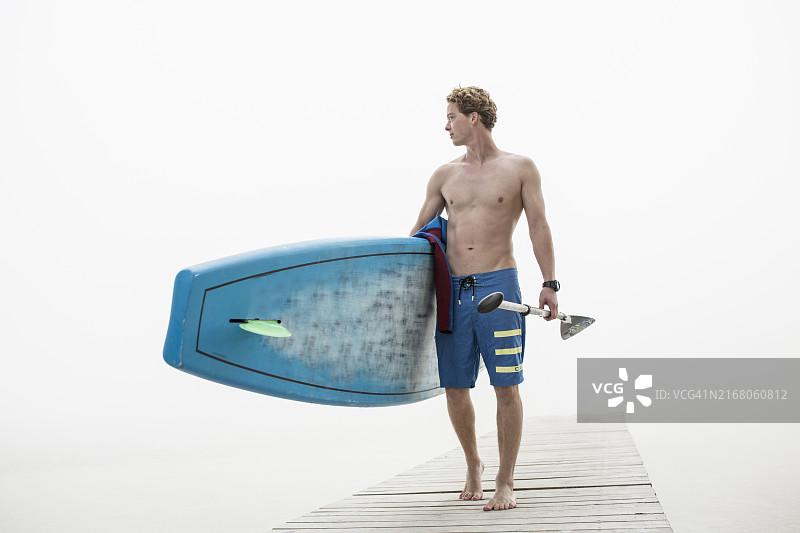 裸着上身的男人在雾天里拿着桨板和船桨在码头上图片素材