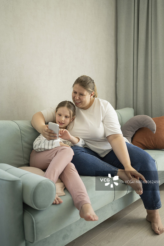 母亲在家用智能手机，女儿坐在沙发上图片素材