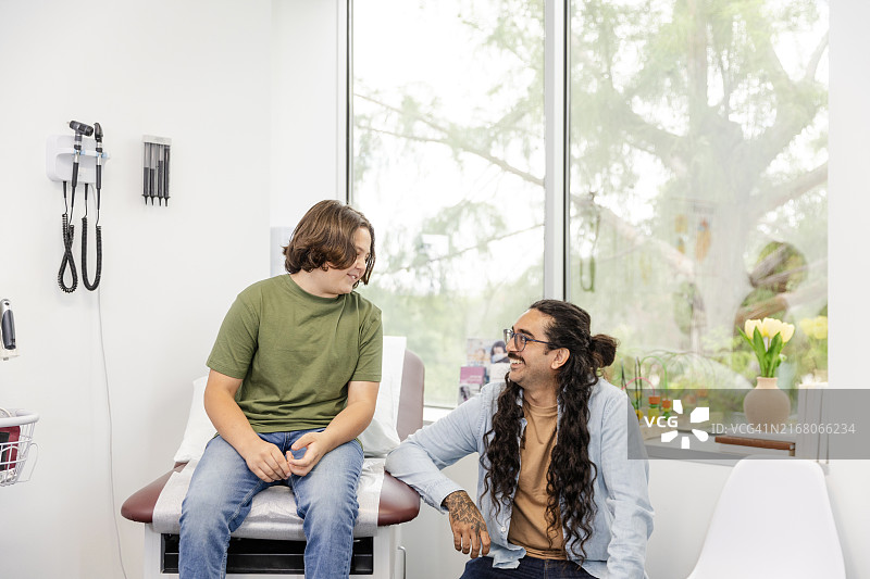 男孩坐在诊察台上和爸爸说话图片素材