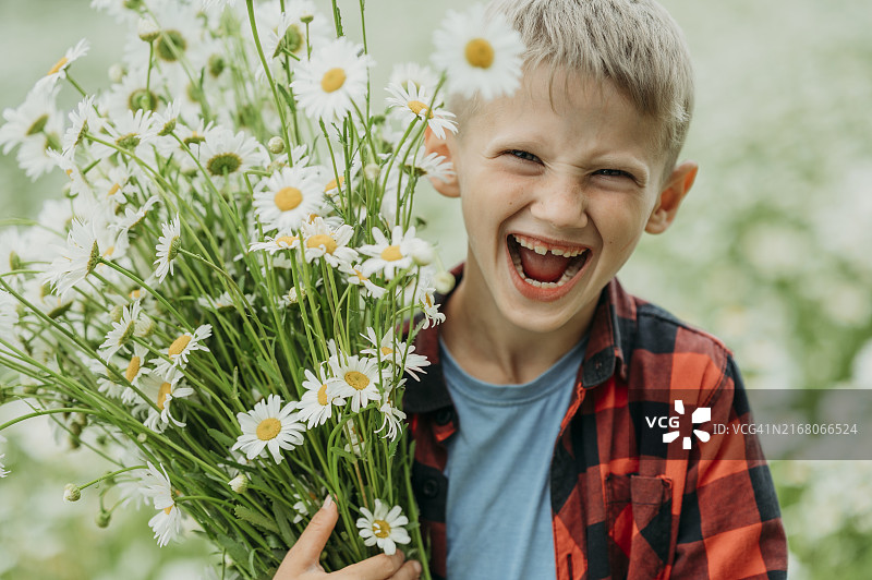 快乐的金发男孩在田野里拿着一束雏菊图片素材