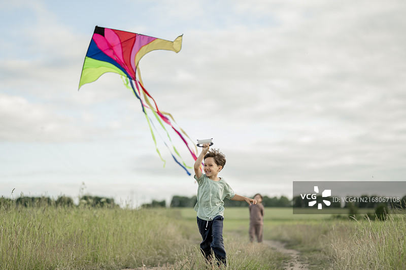 快乐的男孩在奔跑，背景是他的兄弟和风筝图片素材
