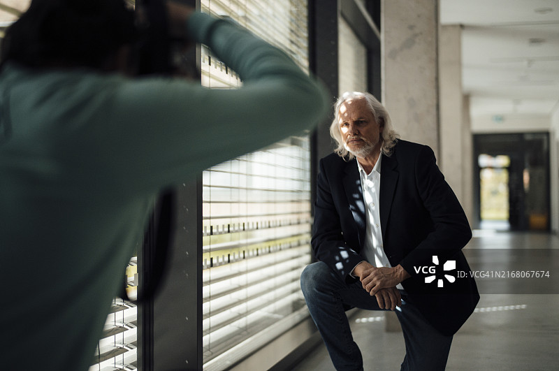 倚靠在窗台上摆姿势让摄影师拍照的年长的男商人图片素材