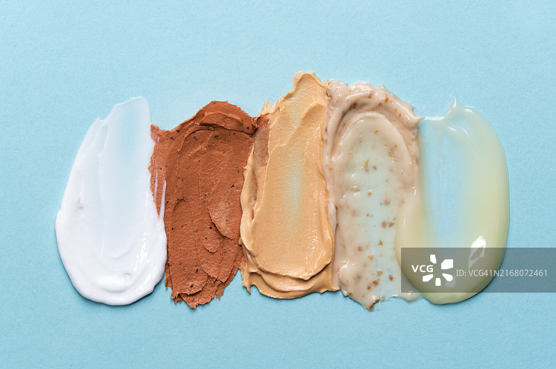 粉色背景上的一组纹理化妆品涂抹痕迹：保湿霜、洁面面膜、沐浴露、去角质磨砂膏和护发素。护肤美容概念，含肽、益生元、神经酰胺、壬二酸的护理化妆品图片素材