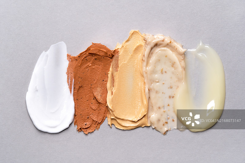 灰色背景上的化妆品涂抹痕迹套装：保湿霜、洁面面膜、沐浴露、磨砂膏和护发素，护肤美容概念图片素材