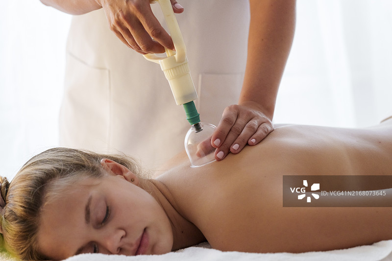 针灸师在养生馆用真空拔罐疗法为少女进行背部护理图片素材