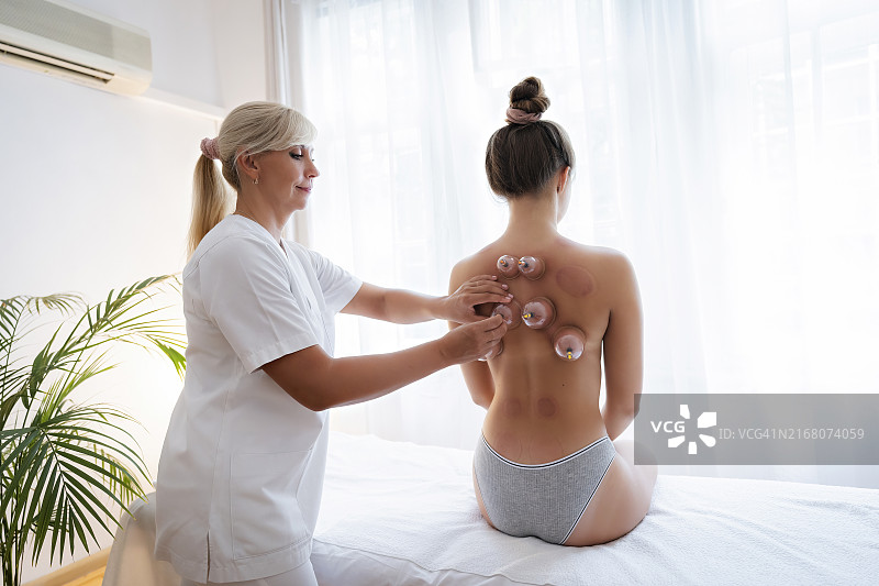 在养生馆，针灸师从少女背部取下真空罐图片素材