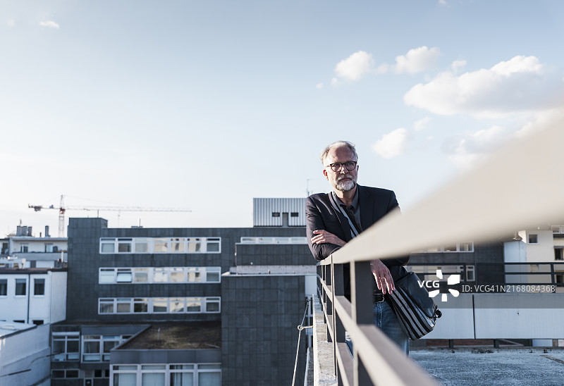沉思的商人倚靠在露台的栏杆上图片素材