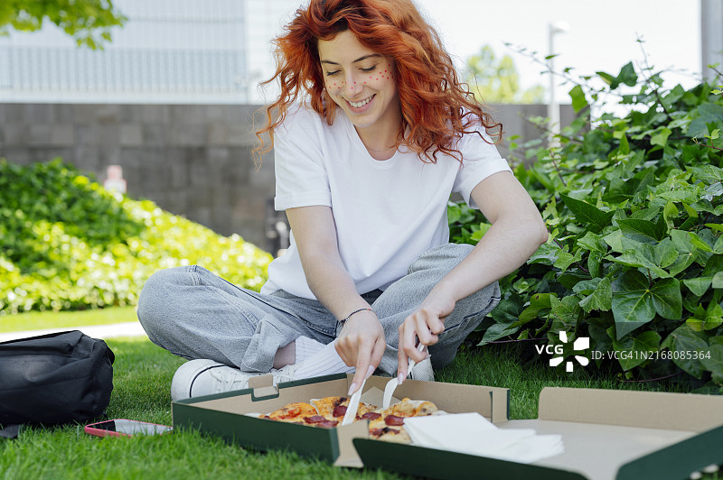坐在公园里切披萨的红发女人图片素材