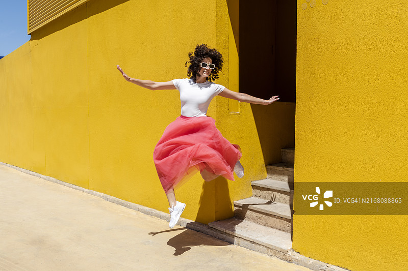 在黄色墙壁附近张开双臂跳跃的女人图片素材