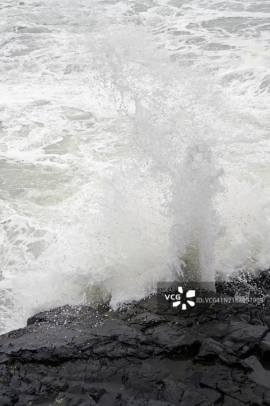在黑色岩石映衬下的白色海浪图片素材