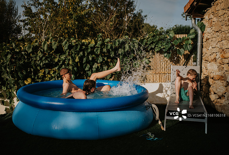 孩子们在阳光明媚的下午，在绿树环绕的后院充气游泳池里享受夏日乐趣图片素材