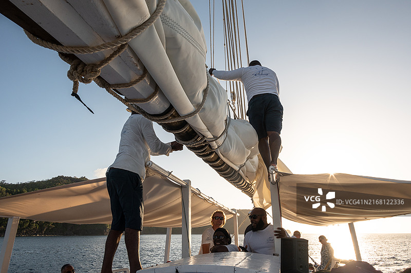 在圣文森特和格林纳丁斯贝基亚岛和多巴哥群岛之间，船员将帆固定在传统帆船的吊杆上图片素材