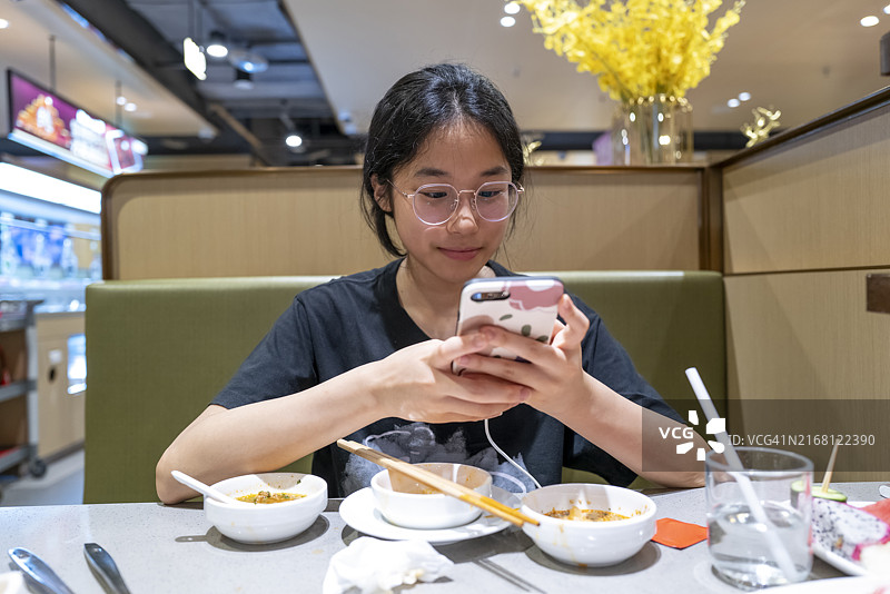 女孩边吃东西边使用手机图片素材