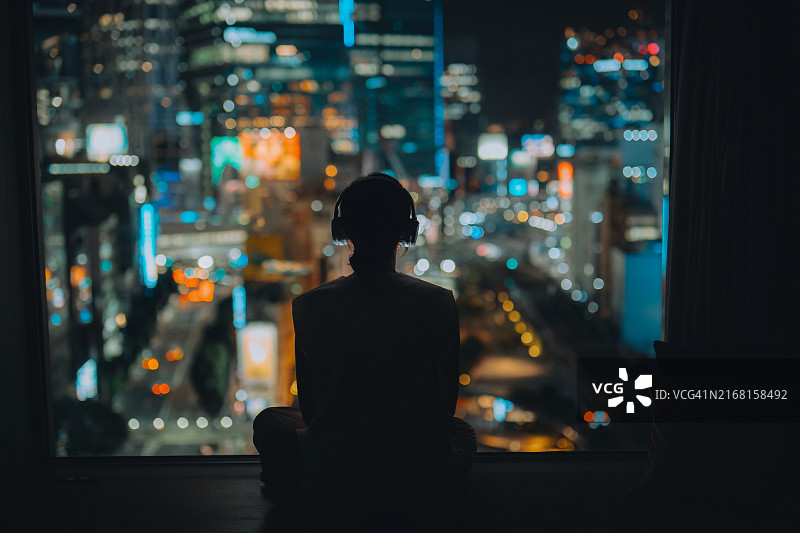 女子在家听音乐，眺望城市夜景的背影图片素材