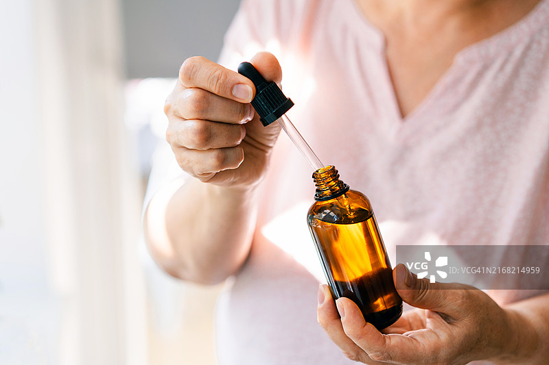 女人拿着滴管和琥珀色玻璃瓶，内含天然精油或有机精华液，身体护理概念图片素材