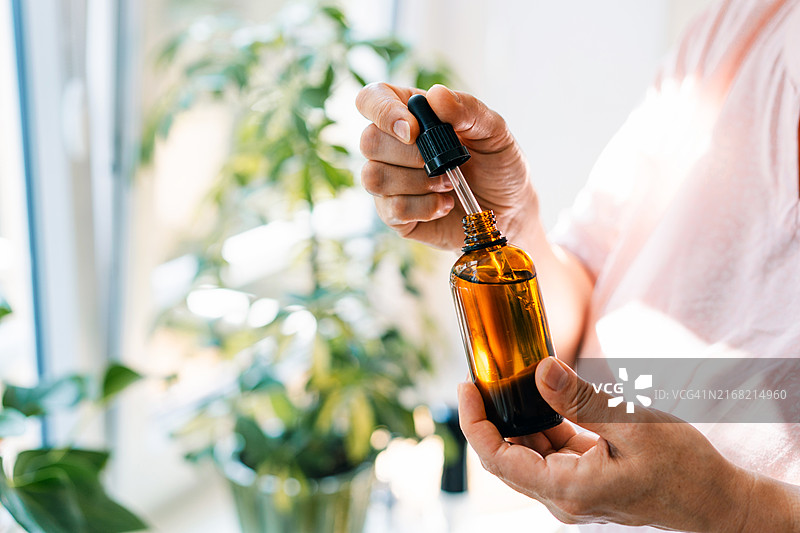 女人拿着滴管和琥珀色玻璃瓶，内含天然精油或有机精华液，身体护理概念图片素材