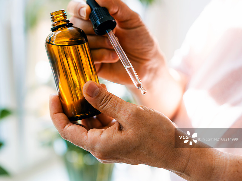 女人手拿滴管和琥珀色精油瓶，身体护理概念图片素材
