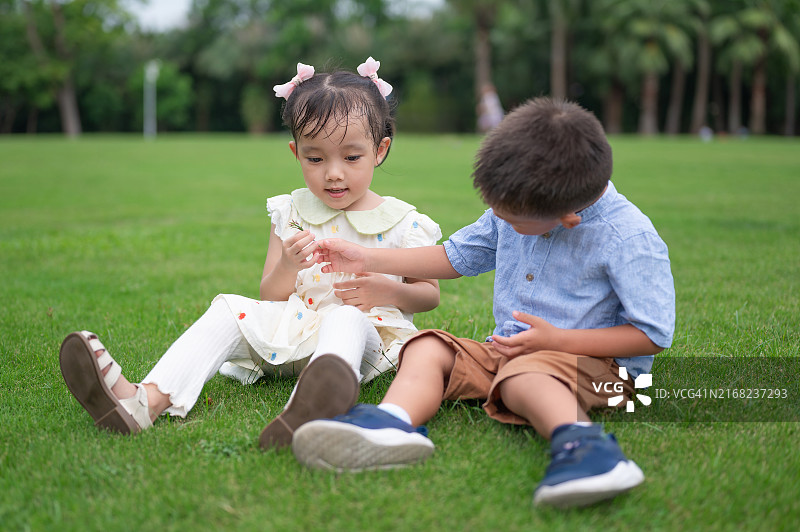 3岁男孩和4岁女孩在草地上玩耍：男孩给他的女性朋友送花图片素材