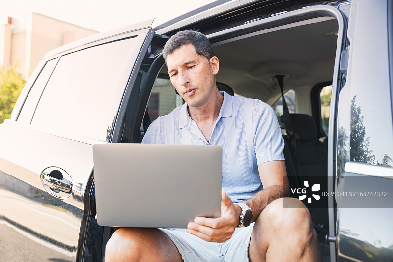 男人坐在车里用笔记本电脑工作。移动办公室概念。图片素材