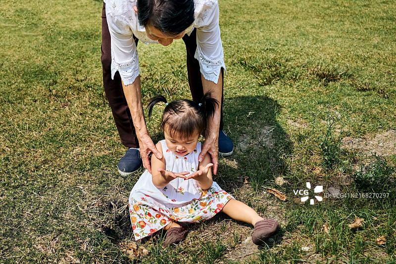 祖母帮助在花园里摔倒的小女孩起身图片素材