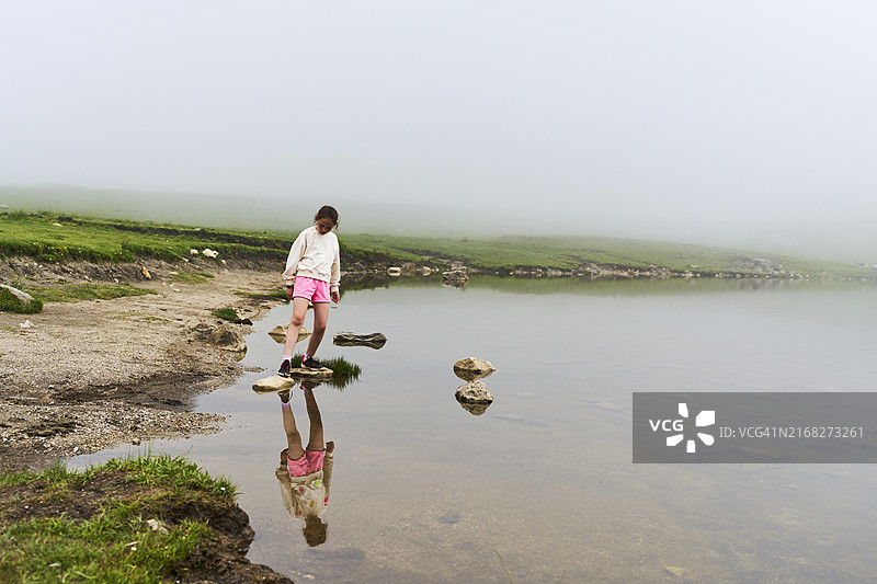 穿着粉色毛衣和短裤的女孩站在科瓦东加湖的岩石上向下看的侧面视角图片素材
