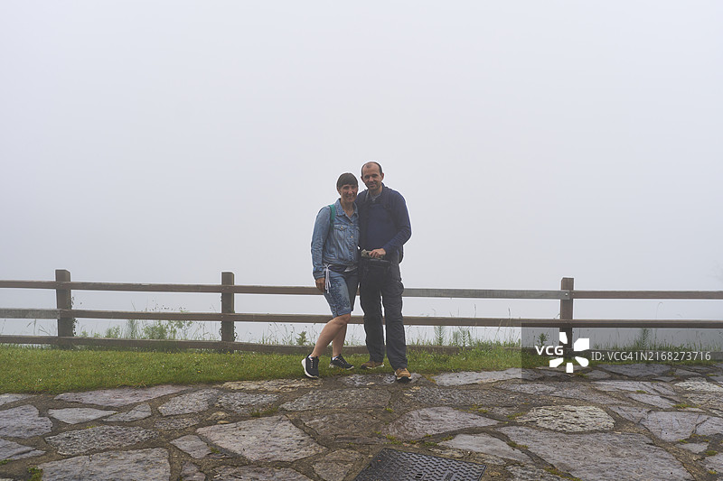一对游客情侣站在土路上，背景是栅栏和雾气的肖像正面照图片素材
