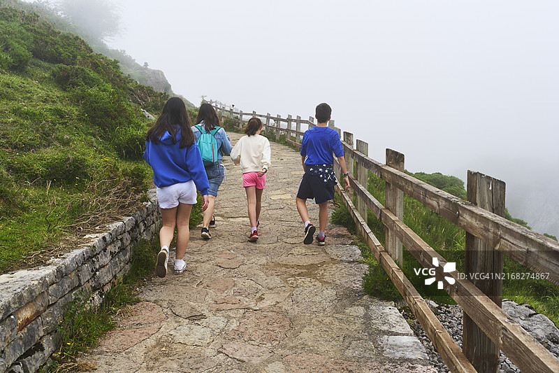带着背包和三个孩子在土路上徒步旅行的女人，背景是雾图片素材