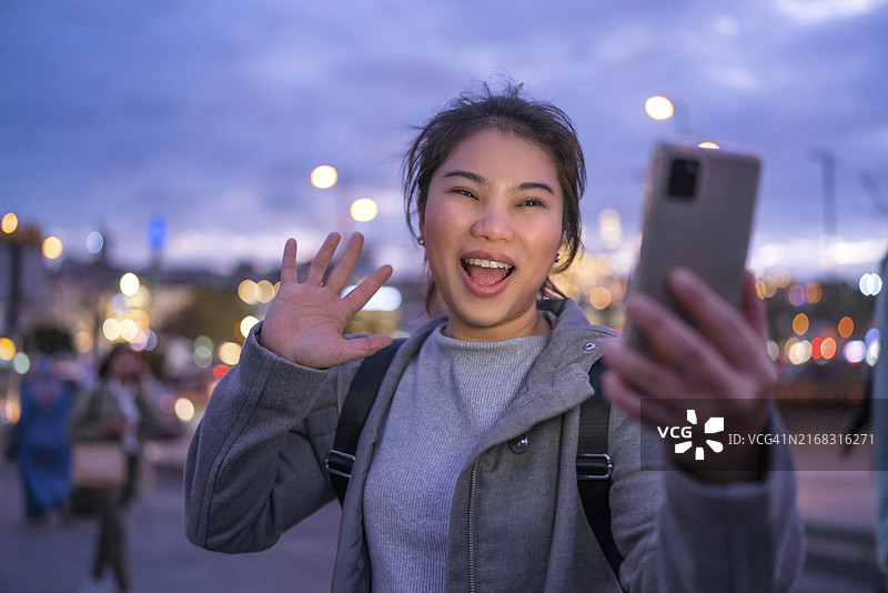独自旅行的亚洲女性在社交媒体上分享旅行瞬间，在加拉塔大桥伊斯坦布尔日落时散步，同时使用智能手机图片素材