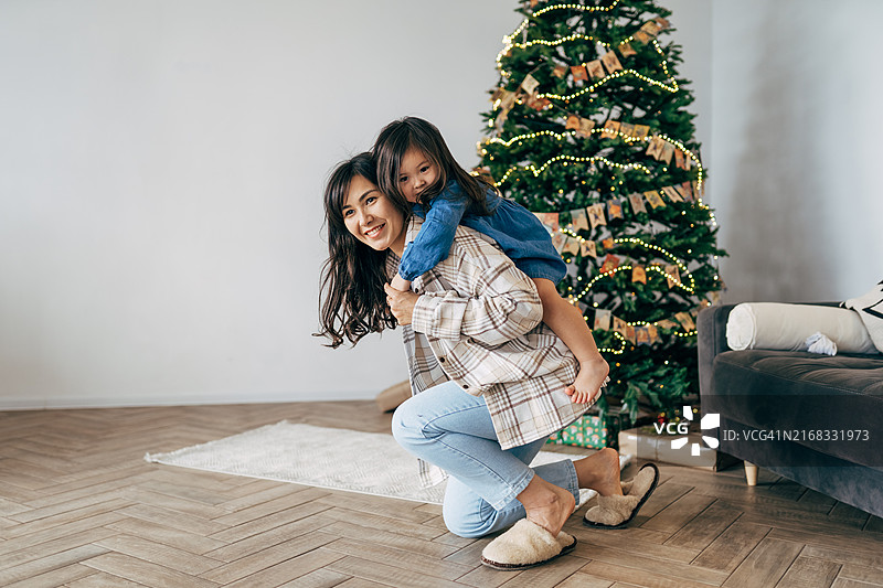 圣诞快乐，节日愉快。快乐的妈妈拥抱可爱的宝宝女儿在圣诞树旁。母亲和孩子在家玩耍。特写。图片素材