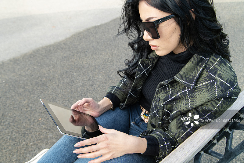 年轻女子在公园长椅上使用平板电脑图片素材