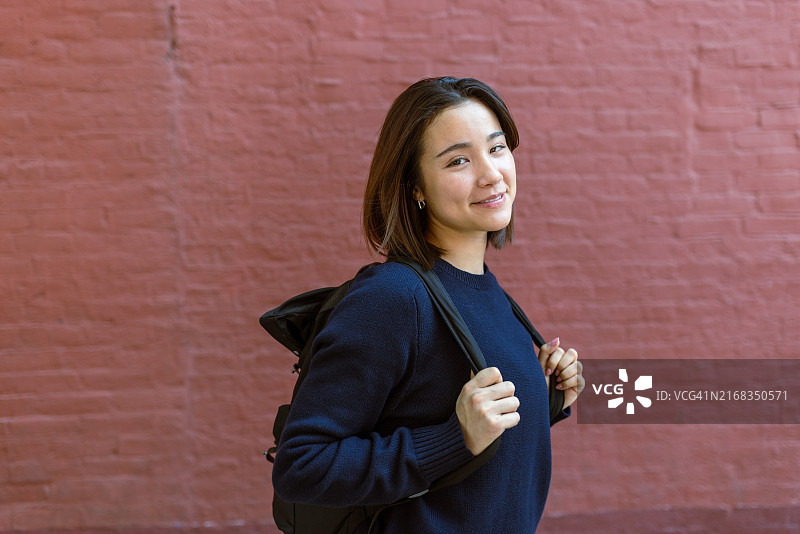 在砖墙前背着背包的微笑学生，白天图片素材