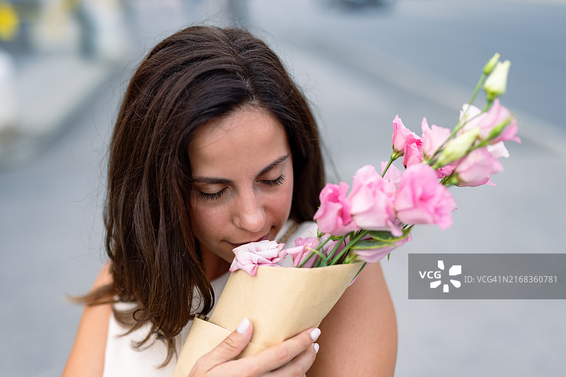 女人嗅着用牛皮纸包裹的粉色鲜花图片素材