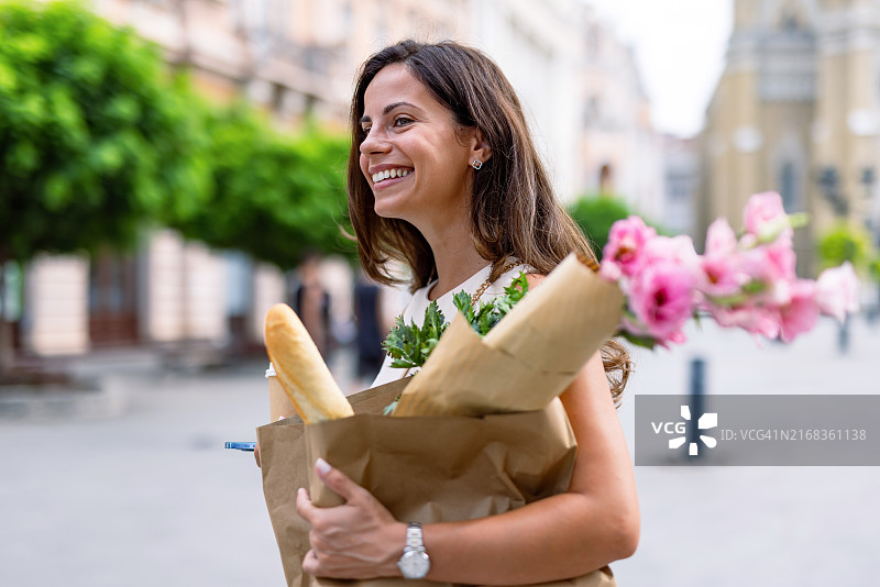 在户外微笑，拿着纸袋杂货的女人图片素材