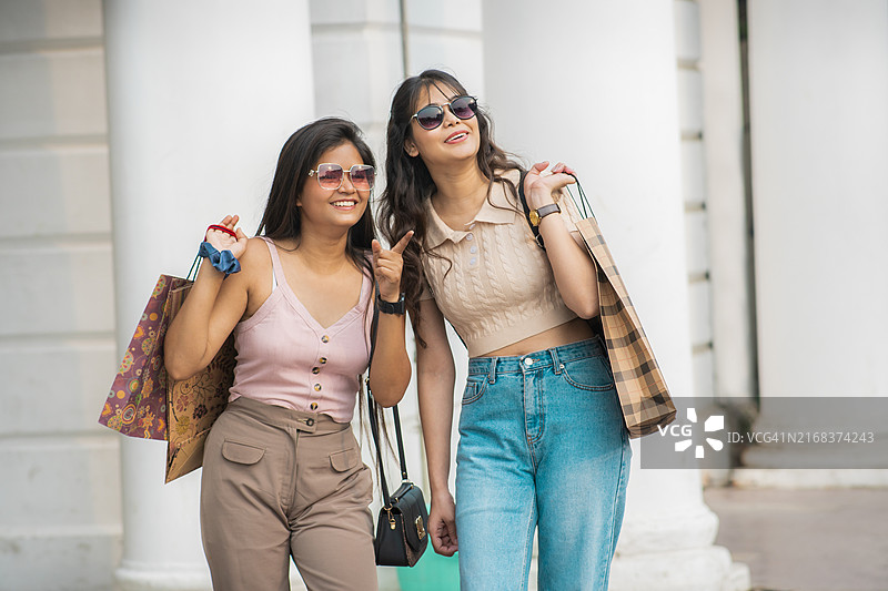 两名年轻女子手提购物袋在城市街道上交谈的快乐肖像照图片素材