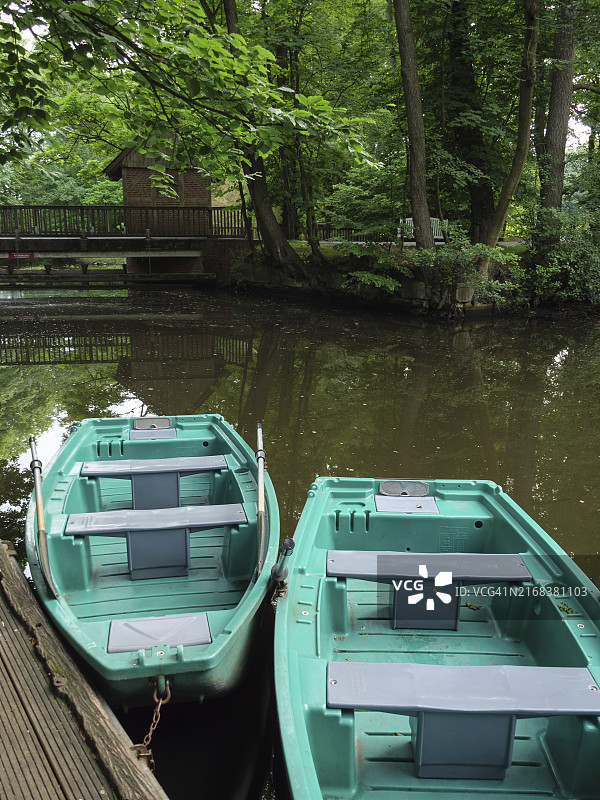 两艘绿色小船停靠在安静的河边木制码头上,周围环绕着茂密的森林,德国北莱茵-威斯特法伦州阿豪斯图片素材