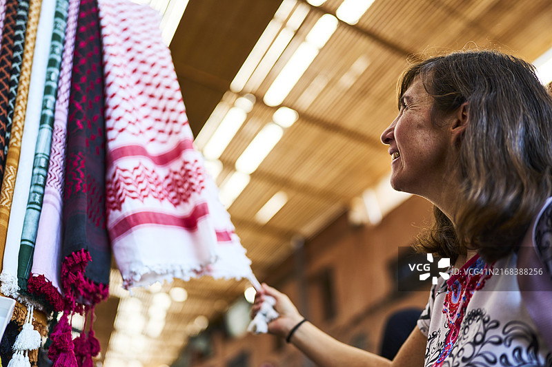 一位面带微笑的女子侧身看着展示的彩色桌布，背景虚化图片素材