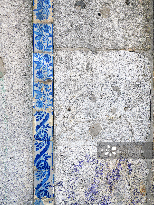 灰色石墙上贴有蓝白色陶瓷砖。葡萄牙波尔图一栋房子的外立面特写。阳光照射下，自然色彩和风化效果。图片素材
